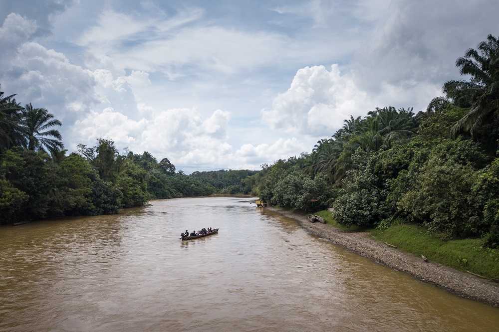 A small boat crossing a wide river with forest on either side