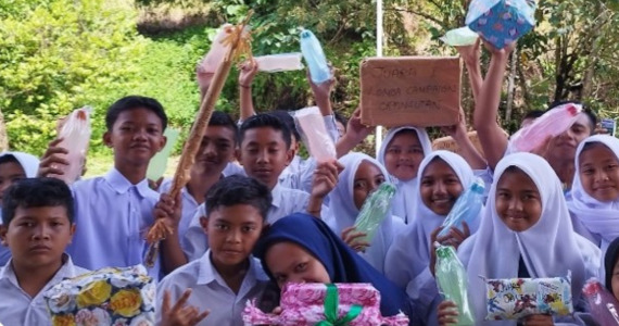 A group of schoolchildren hold up wrapped gifts and smile at the camera
