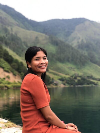 A woman - Lina Rita Silaban - West Toba Landscape Manager - sits beside a lake surrounded by hills
