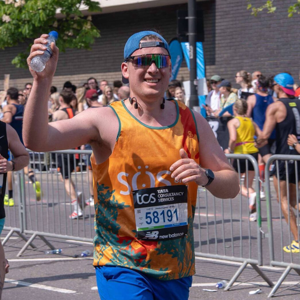 A Team SOS charity runner wearing an orange vest celebrating during the London Marathon.